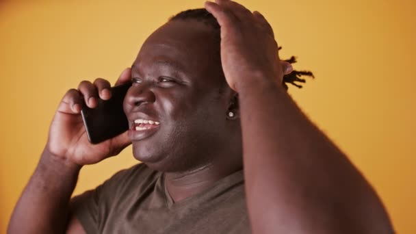 Retrato de un africano conversando por teléfono. Aislado sobre el fondo naranja — Vídeos de Stock