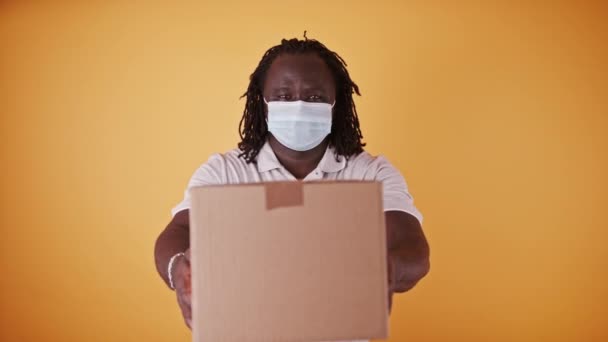 Afrikansk leverans man med ansiktsmask - kurir räckte paketet rutan - kopiera utrymme isolerad — Stockvideo