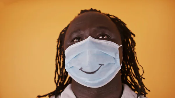 Hombre africano con máscara facial con sonrisa dibujada mirando hacia el cielo con esperanza — Foto de Stock