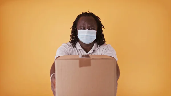 Repartidor africano con máscara facial - mensajero entregando la caja del paquete - espacio de copia aislado — Foto de Stock
