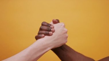 Siyah ve beyaz eller, turuncu arka planda izole bir şekilde el ele tutuşuyorlar. Kapat.