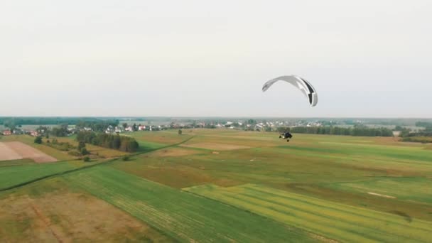 Drohnenschuss eines Paramotor Tandems, das über die grünen Felder fliegt — Stockvideo