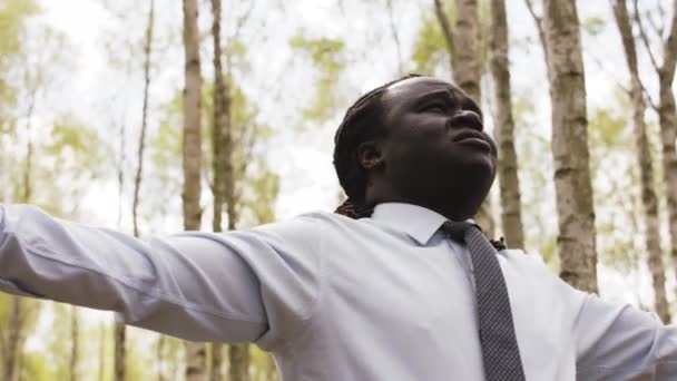Ung afrikansk affärsman med utsträckta händer i skogen — Stockvideo
