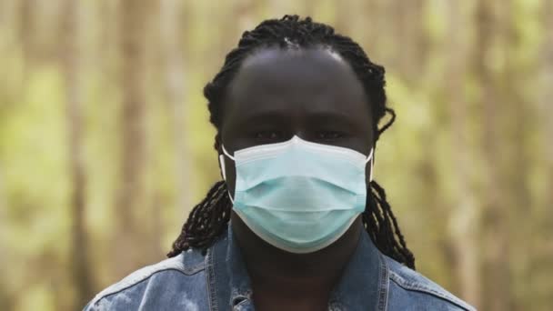 Retrato de un hombre africano con máscara médica en la cara en el parque — Vídeos de Stock