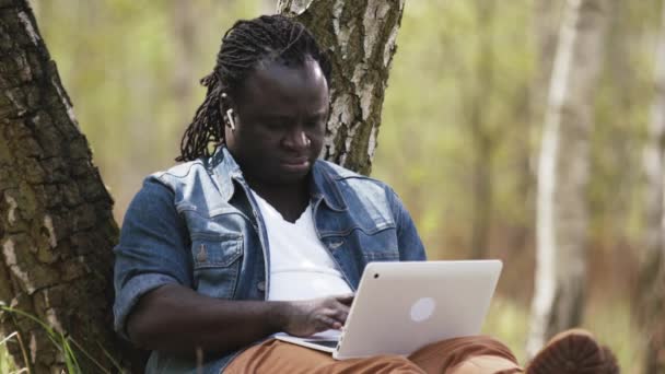Новая норма. Дистанционное обучение на расстоянии. Африканский человек с помощью ноутбука в природе — стоковое видео