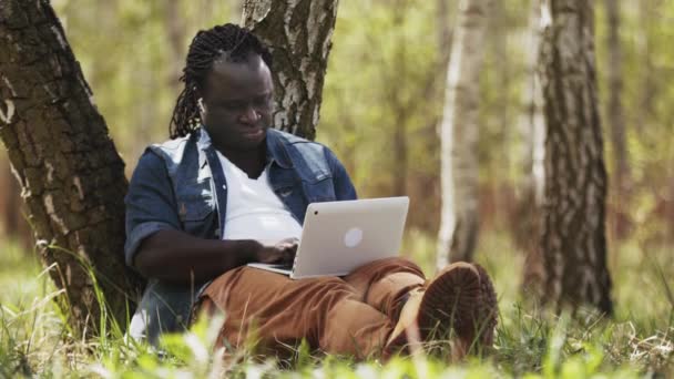 Novo normal. Trabalho remoto ou conceito de ensino à distância. homem africano usando laptop na natureza — Vídeo de Stock
