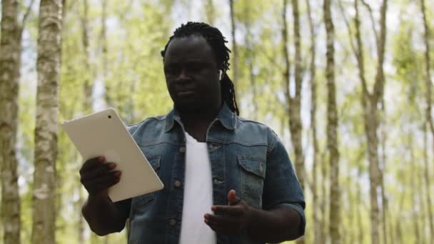 Afrykanin używający tabliczki w lesie. koncepcja technologii bezprzewodowej lub przyszłej — Wideo stockowe