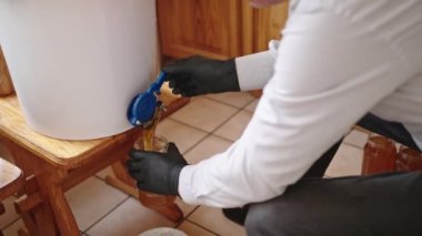 Arı kovanının içi. Arıcı fıçıdaki balı boşaltıyor.