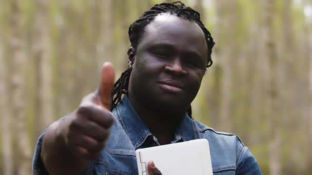 African man with tablet holding a thumb up in the park. Rack focus — Stock Video