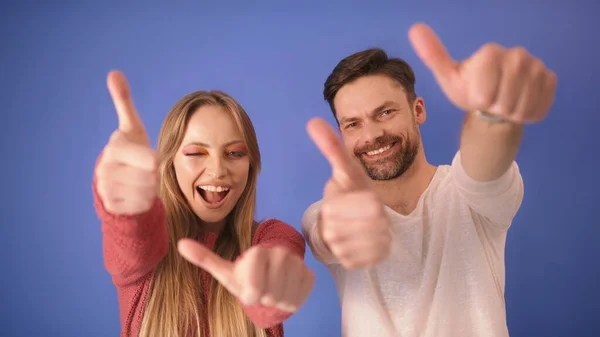 Young happy couple with thumbs up isolated on the blue background. — Stock Photo, Image