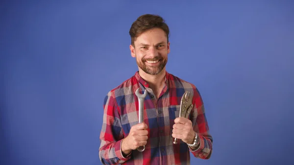 Young man, repairman or handy man holding tools. Isolated on the blue background — Stock Photo, Image