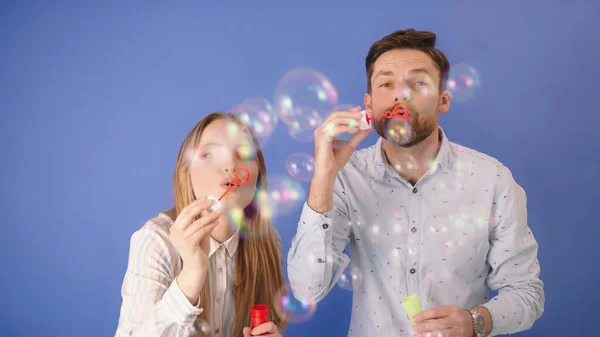 Soap bubbles on CAM. Man and woman are having fun with soap bubbles. Isolated on blue — Stock Photo, Image