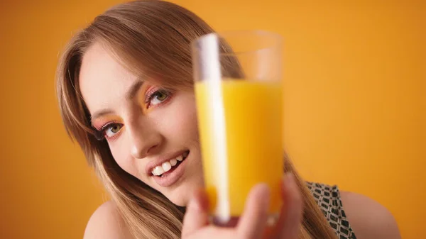 Jonge vrouw met glas sinaasappelsap geïsoleerd over oranje achtergrond — Stockfoto