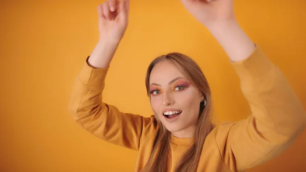 Glückliches blondes Mädchen im Party-Modus tanzt, Hände bewegen sich in der Luft. Vereinzelt auf dem orangefarbenen Hintergrund — Stockfoto