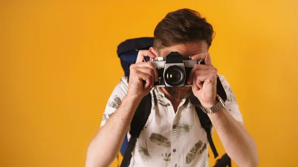 Kavkazský cestovatel s batohem, který se dívá hledáčkem na kameře. Izolované na oranžovém pozadí — Stock fotografie