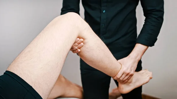 Un joven examinándose la rodilla por un especialista. Flexibilidad de la rodilla fisioterapia —  Fotos de Stock
