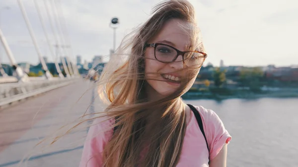 Jonge brunette met bril geniet van winderige dag op de brug. Langzame beweging — Stockfoto