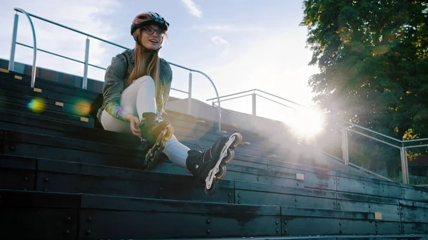 Joven mujer deportiva ajustando patines mientras está sentado en las escaleras en el parque de skate. — Foto de Stock