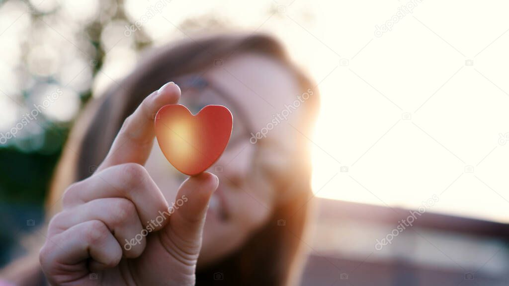 Heart shape in the hand of a beautiful young lady with glasses. Lens flare