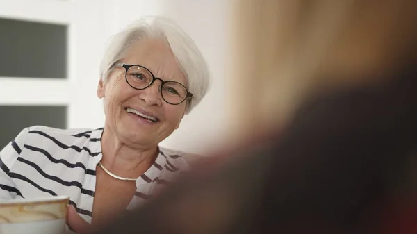 Mujer mayor con gafas y cabello blanco bebiendo café de té y riendo. Concepto de jubilación — Foto de Stock