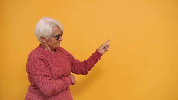 Siwe włosy starsza kobieta w okularach przeciwsłonecznych wskazując palcem na pustej przestrzeni — Zdjęcie stockowe