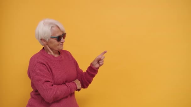 Wanita tua berambut kelabu dengan kacamata hitam menunjuk jari pada ruang kosong — Stok Video