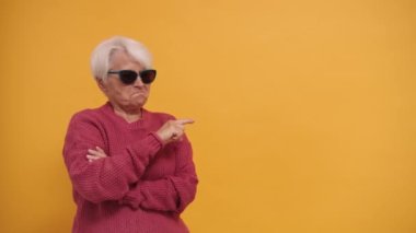 Güneş gözlüklü, modaya uyan, boş alanı işaret eden ve başını sallayan bir büyükanne.