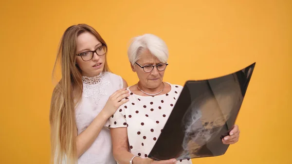 Dos mujeres preocupadas, jóvenes y mayores sosteniendo una radiografía o una resonancia magnética en la cabeza — Foto de Stock