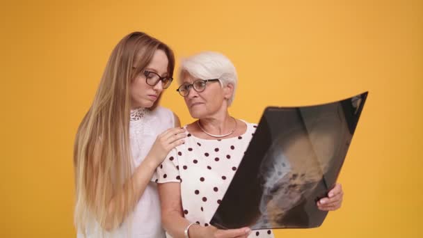 Νεαρή γυναίκα που αντιμετωπίζει ανήσυχη ηλικιωμένη κυρία κρατώντας μια ακτινογραφία o μαγνητική τομογραφία κεφαλής — Αρχείο Βίντεο