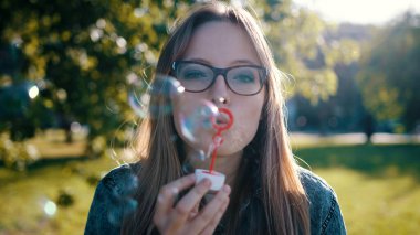 Genç bir kadın doğada sabun köpüğü üflüyor. Parkta gözlüklü mutlu bir esmer kız. 