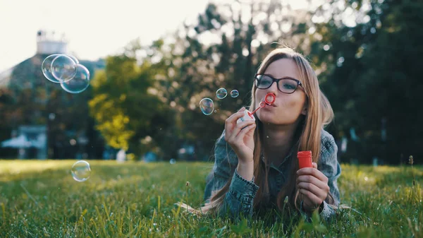Gelukkig jong Kaukasisch vrouw blazen zeepbellen terwijl liggend in het gras in het park — Stockfoto