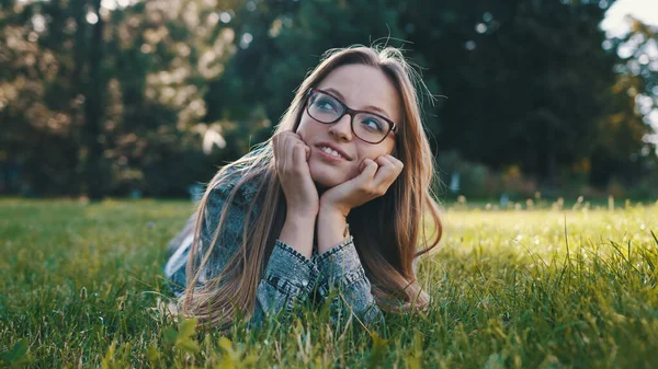 Jonge Kaukasische brunette dagdromend op het gras in het park. Ontspanning in de natuur — Stockfoto