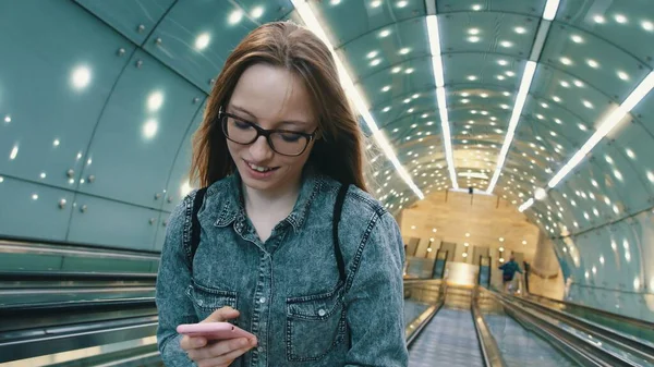 Портрет молодой женщины, использующей смартфон в хорошо освещенном тоннеле — стоковое фото