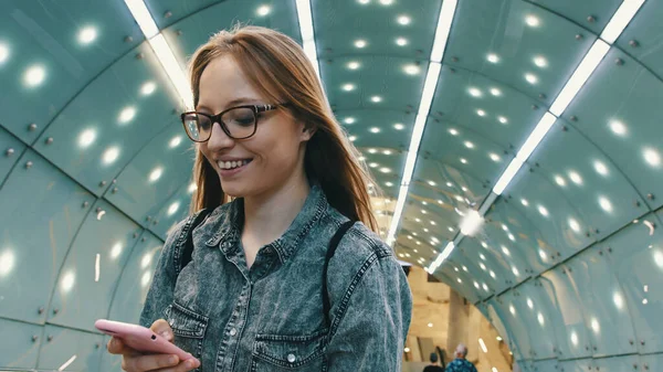 Retrato de mulher branca sorridente usando smartphone em túnel bem iluminado — Fotografia de Stock