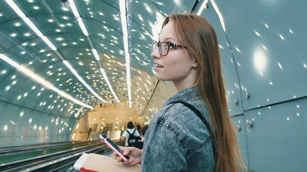 Футуристический портрет молодой женщины с книгами и смартфоном в тоннеле — стоковое фото