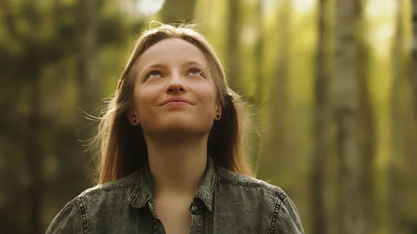 Portret van een jonge blanke vrouw zonder make-up die glimlachend het bos in kijkt — Stockfoto