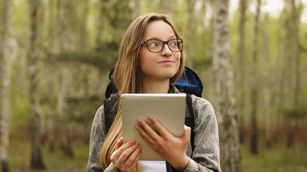 Retrato de jovem turista com mochila e tablet andando na floresta — Fotografia de Stock