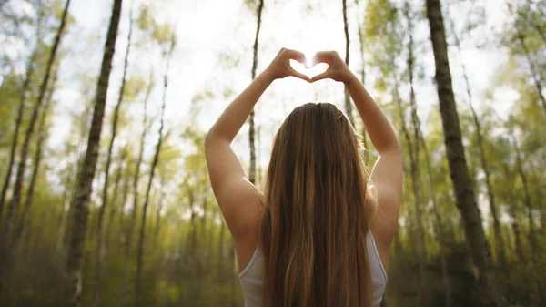 Vrouw inlijstende zon met haar handen in hartvorm. Kopieerruimte — Stockfoto