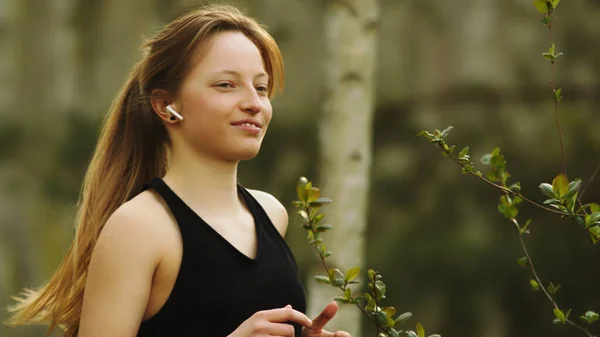 Estilo de vida saudável. Mulher caucasiana jovem com fones de ouvido sem fio correndo na floresta. Retrato tirado — Fotografia de Stock