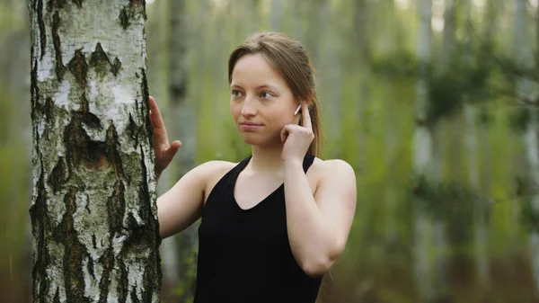 Jonge blanke vrouw in de natuur. De muziek beluisteren op de draadloze hoofdtelefoon en de boomschors aanraken. Langzame beweging. — Stockfoto
