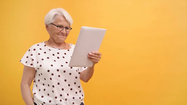 Mujer mayor teniendo una videollamada en la tableta. Aislado sobre el fondo naranja — Foto de Stock