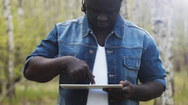 Un hombre africano usando la tableta en el bosque. concepto de tecnología inalámbrica o futura. — Foto de Stock