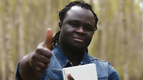 Afričan s tabletou, držící palec v parku. — Stock fotografie
