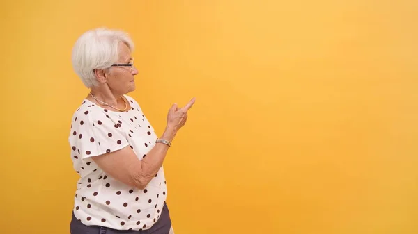 Mujer mayor señalando con el dedo el espacio publicitario vacío. Fondo naranja — Foto de Stock