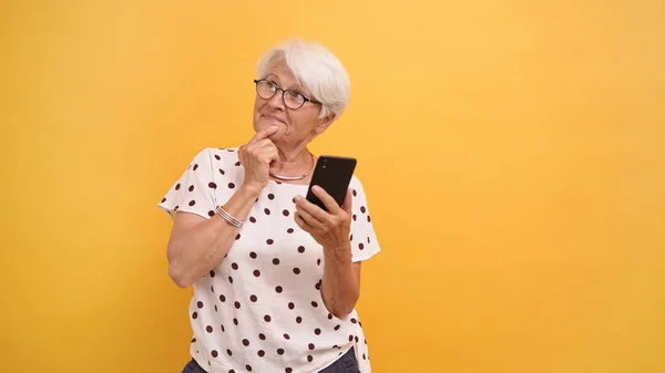 Старшая женщина держит смартфон и думает о новой должности в социальных сетях — стоковое фото