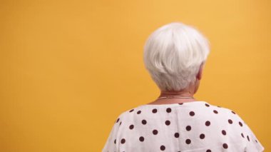 Turuncu arka planda izole edilmiş yaşlı bir kadının arka görüntüsü