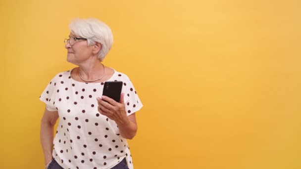 Старша жінка тримає смартфон і дивиться на сторону, сподіваючись побачити відвідувача — стокове відео