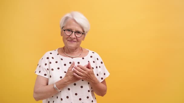 Ηλικιωμένη γυναίκα βάζει τα χέρια της πάνω από τη ζέστη με χαμόγελο. Συναισθήματα απομονωμένα σε πορτοκαλί φόντο — Αρχείο Βίντεο