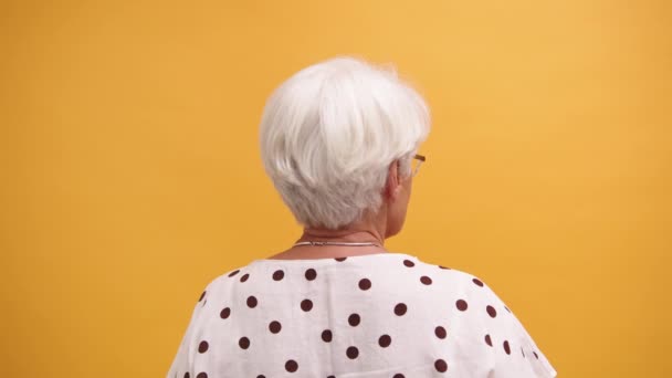 Vista posterior de una mujer mayor aislada sobre el fondo naranja — Vídeo de stock