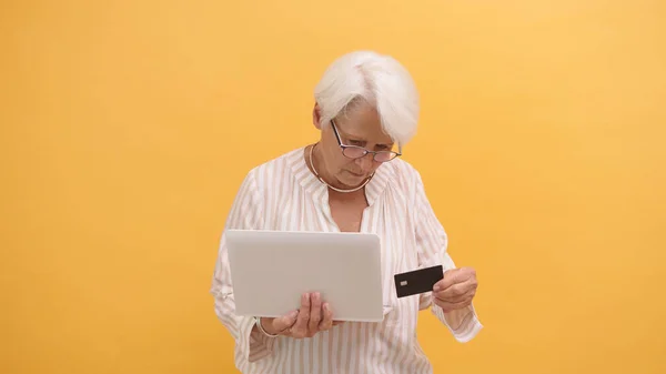 Запутавшаяся пожилая женщина пытается вставить кредитку в ноутбук. Интернет-магазины — стоковое фото